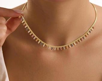May include: Gold-toned necklace with a delicate chain and small, colorful rectangular pendants. The pendants feature a variety of colors, including pink, blue, and yellow. The necklace is worn around the neck.