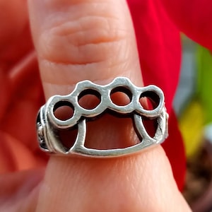 Op de afbeelding: Een zilveren ring met een knokkelstoot-ontwerp. De ring wordt aan een vinger gedragen.