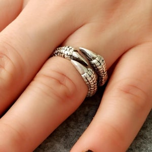 May include: Silver ring with a claw design. The ring is worn on a finger.