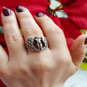 Hand wearing statement winged goddess ring, red floral background.