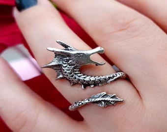 May include: A silver dragon ring with a coiled tail. The dragon's head is facing forward with its mouth open.