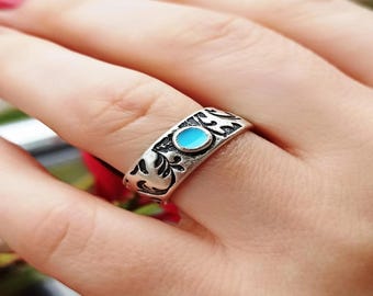 Peut inclure: Une bague en argent avec une pierre ovale bleu clair au centre. La bague présente un motif gravé orné autour de l'anneau. La bague est présentée sur un doigt.