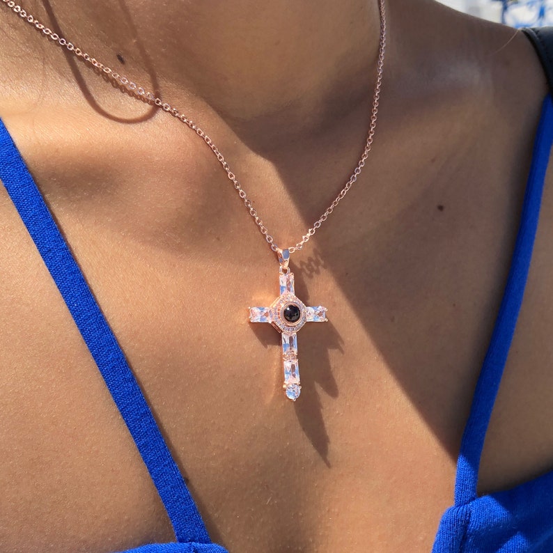 K&ouml;nnte beinhalten: Eine Halskette aus Ros&eacute;gold mit einem Kreuzanh&auml;nger, der einen schwarzen Stein in der Mitte und klare Zirkonia-Steine an den R&auml;ndern hat.