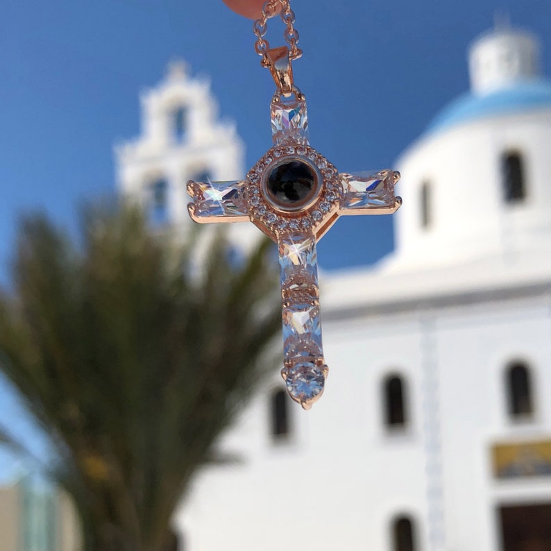 K&ouml;nnte beinhalten: Eine Halskette mit einem Kreuz-Anh&auml;nger aus ros&eacute;gold, besetzt mit klaren Zirkonia-Steinen. Der Anh&auml;nger hat einen runden Mittel-Stein mit einer schwarzen "Ich liebe dich"-Projektion.