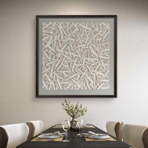 May include: Abstract artwork in a dark frame. The art piece features a textured pattern of white and beige shapes on a gray background. The artwork is displayed above a dining table set with plates, glasses, and silverware.