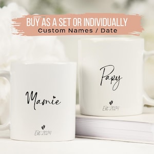 May include: Two white ceramic mugs with black lettering. The mug on the left says "Mamie Est. 2024" and the mug on the right says "Papy Est. 2024".