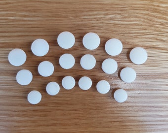 May include: A collection of 18 white round pills on a wooden surface.