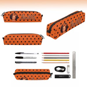 May include: An orange pencil case with black polka dots, featuring a cartoon character with curly hair and the name Judith printed in white script. The set includes various pens, pencils, a USB drive, a charging cable, and a 6-inch metal ruler.