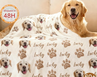 May include: A cream-colored blanket featuring a repeating pattern of golden retriever faces, paw prints, and the word "Lucky" in brown. A golden retriever dog is lying on the blanket. The blanket is made in the USA.