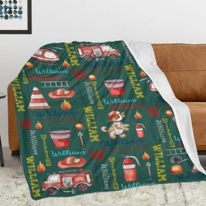 May include: A green blanket with a repeating pattern of fire trucks, fire hats, and the name "William" in a playful font. The blanket also features a cartoon dog in a firefighter's hat and other fire-related illustrations.