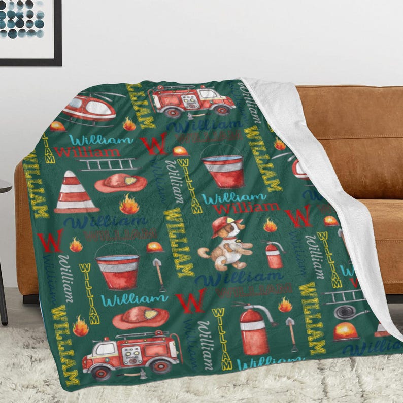 May include: A green blanket with a repeating pattern of fire trucks, fire hats, and the name "William" in a playful font. The blanket also features a cartoon dog in a firefighter's hat and other fire-related illustrations.