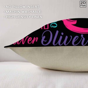 K&ouml;nnte beinhalten: Ein dekorativer Kissenbezug aus hochdichtem Leinen mit einem schwarzen oberen Bereich, der den Text Oliver in violetter Schreibschrift und rosa Akzenten zeigt. Der untere Bereich ist einfarbig beige. Der Text auf dem Bild lautet NO PILLOW INSERT, MACHIN WASHABLE und HIGH DENSITY LINEN.
