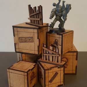 May include: A set of six wooden crates with warning and skull and crossbones labels. The crates are stacked in a pyramid shape with a miniature grey space marine figure standing on top. The crates are made of brown wood with black lettering and designs.