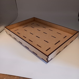 Può includere: Un vassoio rettangolare in legno con finitura marrone chiaro. Il vassoio ha un bordo rialzato e una serie di ritagli rettangolari distanziati uniformemente sulla base. Gli angoli sono uniti con precisione e il design è semplice e funzionale.