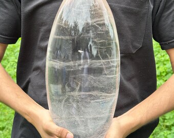 May include: A large, clear quartz crystal shaped like an egg. The crystal is smooth and has a slight shimmer to it.