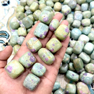 Peut inclure: Une collection de pierres polies présentant une base vert pâle avec des inclusions minérales distinctes de couleur magenta et violette. Chaque pierre possède une surface lisse et polie avec une forme arrondie et irrégulière.