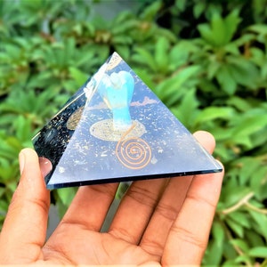 Könnte beinhalten: Eine klare Kristallpyramide mit einer goldenen Spirale und einem blauen und weißen Bild im Inneren. Die Pyramide liegt auf einer Hand.