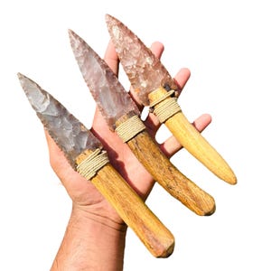May include: Three flint arrowheads with wooden handles and leather wrappings. The arrowheads are translucent and have a pink and white color.