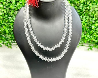 Puede incluir: Un collar mala de cristal transparente con un borla roja. El collar está hecho de cuentas redondas y se muestra en un maniquí negro.
