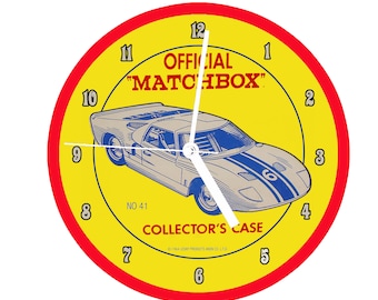 May include: A yellow and red circular clock with a white face and black numbers. The clock features a blue and white race car with the text "OFFICIAL "MATCHBOX" NO 41 COLLECTOR'S CASE © 1964 LESAY PRODUCTS AND CO. LTD."