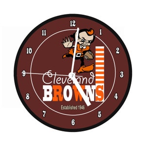 Könnte beinhalten: Eine braune und weiße Uhr mit dem Logo der Cleveland Browns. Das Logo zeigt einen Comic-Elf, der einen Football hält, mit den Worten "Cleveland Browns" und "Gegründet 1946".