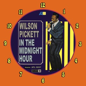 May include: A vintage vinyl record clock featuring a portrait of Wilson Pickett, the album title "In The Midnight Hour", and the Atlantic Records logo. The clock face is surrounded by a bright orange background with black numbers.