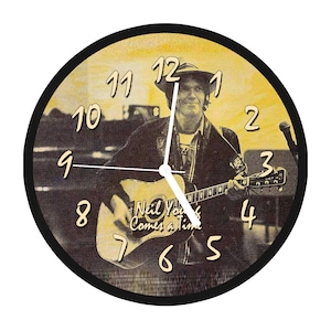 Puede incluir: Un reloj redondo con marco negro y esfera amarilla. El reloj presenta una imagen de Neil Young tocando la guitarra. La esfera del reloj tiene números y manecillas negros. El texto "Neil Young Comes a Time" está impreso en la esfera del reloj.