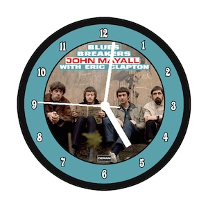 May include: Round wall clock featuring the band Blues Breakers with John Mayall and Eric Clapton. The clock face is light blue with black numbers and hands. The band members are seated in front of a wall. The clock has a black border.