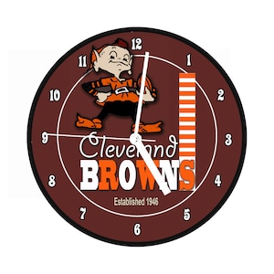 Könnte beinhalten: Eine braune und orangefarbene Uhr mit einem Comic-Elf, der einen Football hält. Das Zifferblatt der Uhr zeigt die Worte "Cleveland Browns" und "Established 1946".