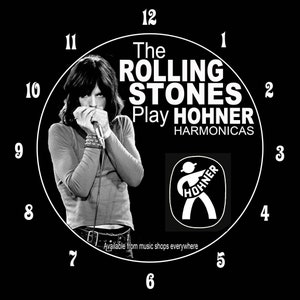 May include: Black and white clock featuring a photo of a musician playing a harmonica. The clock face has the text "The Rolling Stones Play Hohner Harmonicas" and a Hohner logo. The clock numbers are in a circle around the image.