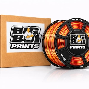 May include: A brown cardboard box and a black spool of orange and yellow filament for 3D printing. The spool has the text "BIG BOI PRINTS" and a logo. The box also has the "BIG BOI PRINTS" logo.
