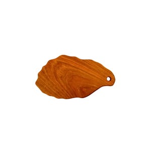 May include: A wooden cutting board with a unique, irregular shape and a small hole in the handle. The board is made of light brown wood with a natural grain pattern.