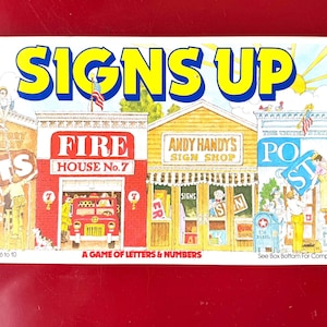 May include: A vintage board game box titled "SIGNS UP" with colorful illustrations of buildings, including a fire station and a sign shop. The game is designed for 2 to 4 players, ages 6 to 10. The box is on a red surface.