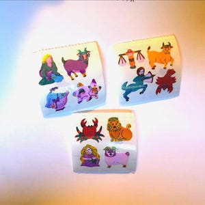 May include: Three sheets of colorful stickers featuring zodiac signs. Each sticker sheet has a white background and displays various astrological symbols, including a goat, bull, and crab. The stickers are in vibrant colors.