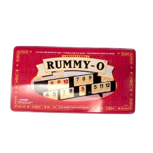 May include: A red collector's edition Rummy-O game set in a rectangular tin. The game includes tiles with numbers and a complete book of rules. The game's name, "Rummy-O," is displayed prominently on the box.