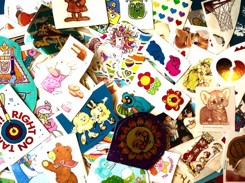 Peut inclure: Une collection d'autocollants vintage avec divers motifs. Les autocollants pr&eacute;sentent une licorne, des fleurs, des animaux et des personnages de dessins anim&eacute;s. Certains autocollants comportent du texte, et la palette de couleurs est vari&eacute;e, avec des teintes vives et pastel.