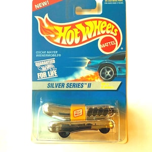 May include: A Hot Wheels Silver Series II toy car, the Oscar Mayer Wienermobile, in its original packaging. The packaging is blue with the Hot Wheels logo and the text "NEW!" and "DIE CAST METAL PARTS. FOR AGES OVER 3 YEARS."