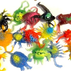 May include: A collection of colorful, plastic toy creatures in various shapes and sizes. The toys are in shades of green, red, yellow, blue, and orange. Some have multiple legs, while others have antennae or other appendages. The toys are likely vintage or retro.