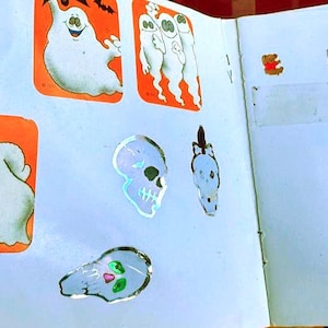 May include: A collection of Halloween-themed stickers, including ghosts, skulls, and bats, in orange and white. Also, a variety of small bear stickers in different colors are visible on a white background.