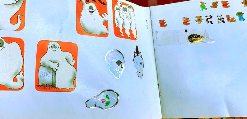 May include: A collection of Halloween-themed stickers, including ghosts, skulls, and bats, in orange and white. Also, a variety of small bear stickers in different colors are visible on a white background.