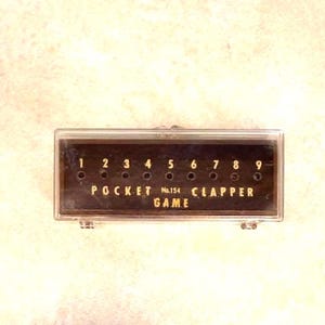 May include: A vintage Pocket Clapper Game in a clear plastic case. The game has a dark brown background with the numbers 1 through 9 and the words "POCKET No.154 CLAPPER GAME" in gold lettering.