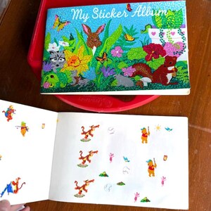 May include: A vintage sticker album with a glittery blue cover featuring the text "My Sticker Album" and a colorful illustration of woodland creatures. The open pages display various stickers of cartoon characters.