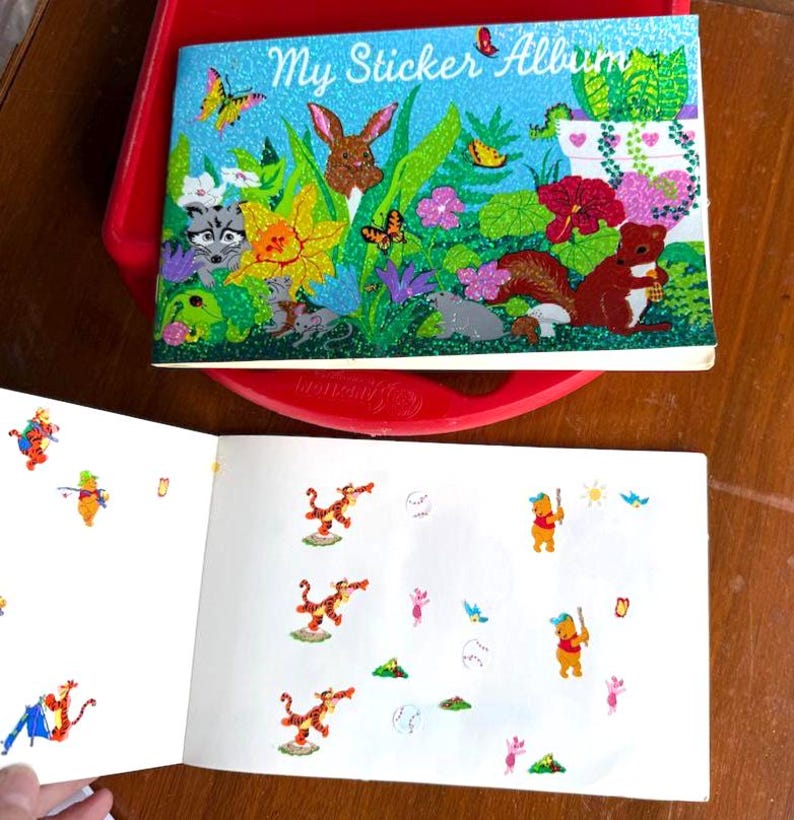 May include: A vintage sticker album with a glittery blue cover featuring the text "My Sticker Album" and a colorful illustration of woodland creatures. The open pages display various stickers of cartoon characters.