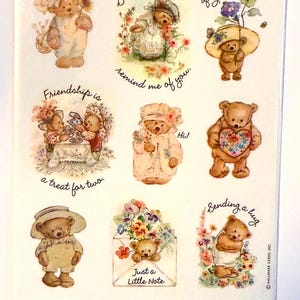 May include: A sheet of stickers featuring teddy bears in various outfits and poses. The bears are surrounded by flowers and have phrases like "Hello!" and "Just a Little Note." The stickers are in a clear plastic package.