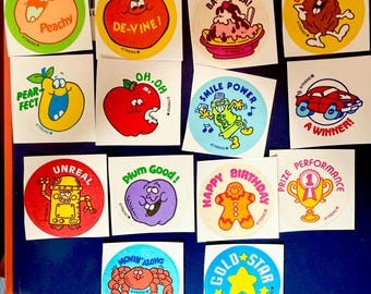 May include: A collection of vintage stickers with various cartoon characters and phrases. The stickers feature images of fruits, desserts, and other whimsical designs. Text includes "Peachy", "De-Vine!", "Ba-Nanza!", "Crackin' Good!", "Unreal", and "A Winner!"