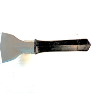 May include: A black and gray scraper tool with a long, black handle and a wide, angled blade. The tool is designed for scraping surfaces and has a sturdy construction.