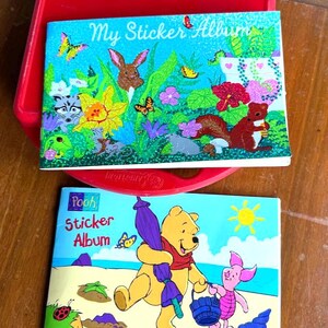 May include: Two sticker albums with colorful illustrations. One album features a rabbit, squirrel, and butterflies with the text "My Sticker Album." The other album has Winnie the Pooh and Piglet with the text "Pooh Sticker Album."