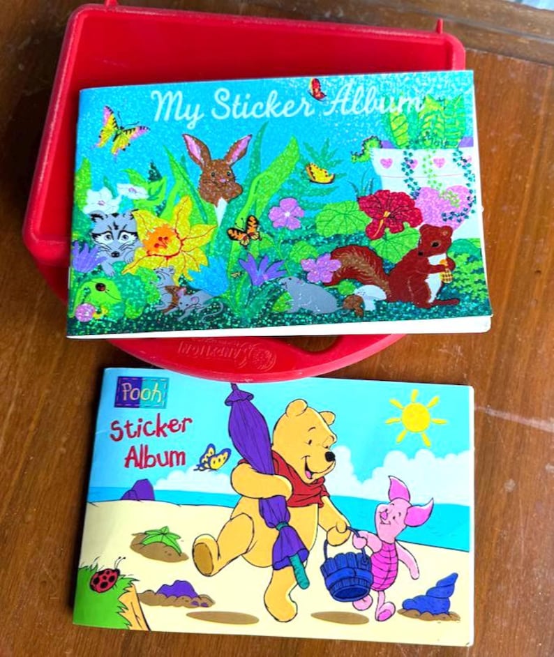May include: Two sticker albums with colorful illustrations. One album features a rabbit, squirrel, and butterflies with the text "My Sticker Album." The other album has Winnie the Pooh and Piglet with the text "Pooh Sticker Album."