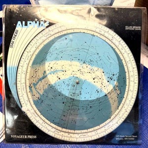 May include: A vintage "Alpha Star Finder" by Gilles Menard and Anthony Davis. The star chart features a blue and white celestial map with constellations and a rotating dial. The cover is black with white text and a Voyager Press logo.