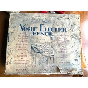 May include: Vintage Vogue Electric Pencil box with illustrations and text. The box is tan with blue text and drawings. Text includes "Writes Electrically in all beautiful COLORS: Gold, Silver, Green, Blue, Red." and "IDEAL For Marking Your POSSESSIONS."